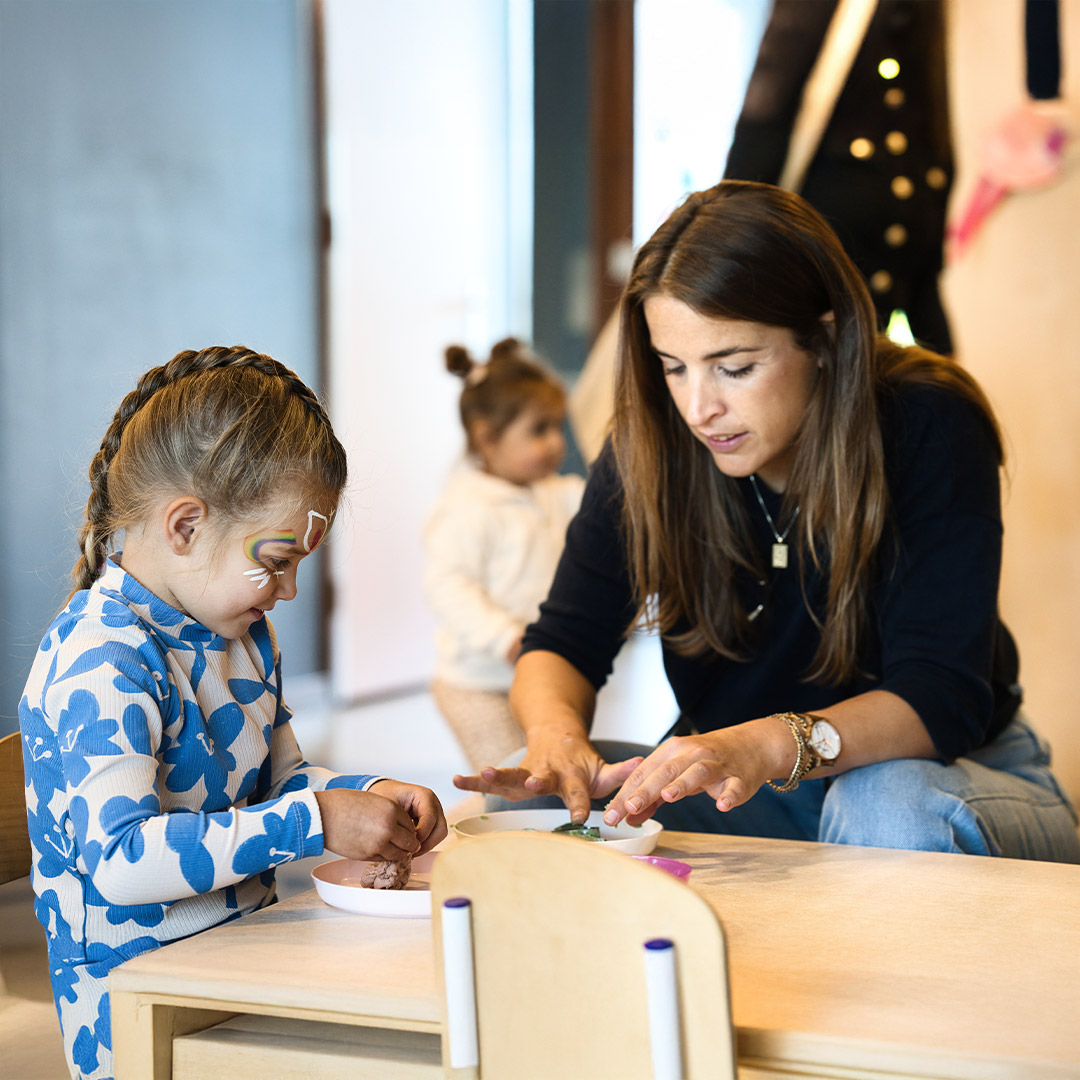 Een pedagogisch medewerker helpt een kind met een kliederactiviteit tijdens een Kids Lodge event