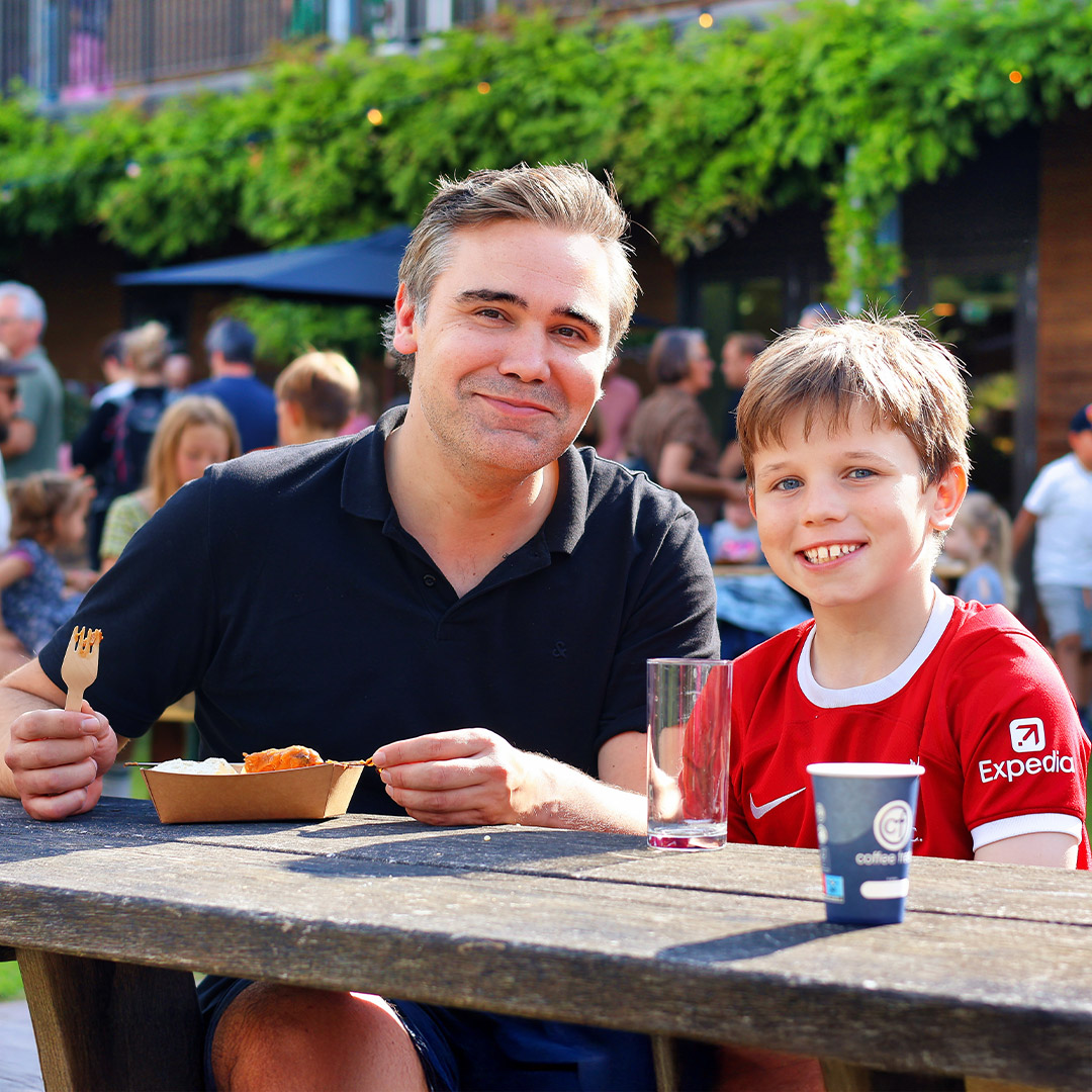 Vader en zoon eten een kipspiesje tijdens een Kids Lodge event
