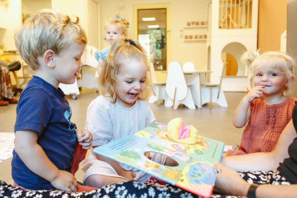Pedagogisch medewerker leest een boek voor aan peuters op locatie In de Rups in Zeist