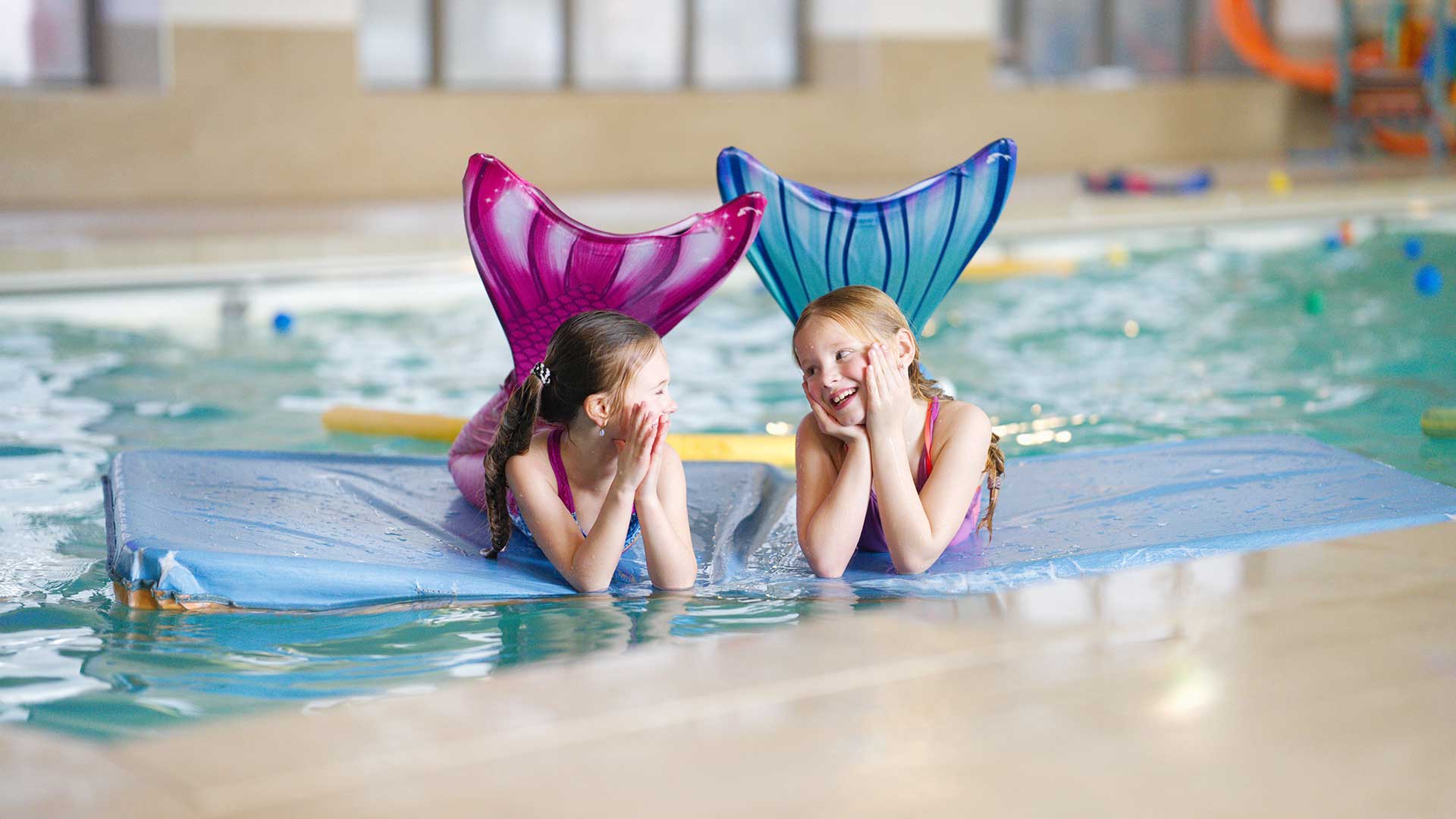 Twee meiden verkleed als zeemeermin drijven op een drijfmat in het water van het zwembad in Houten