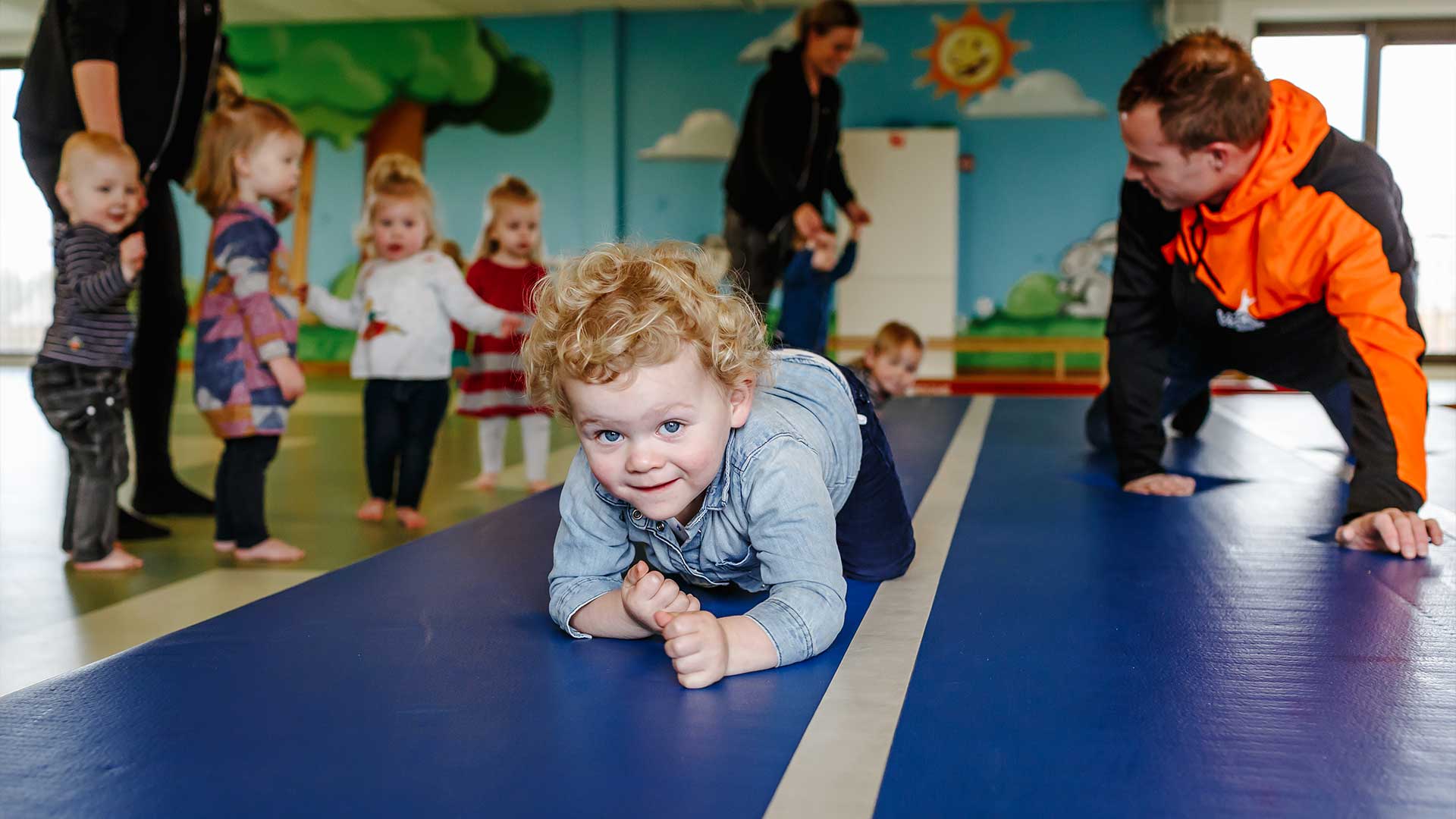 Kleuters en begeleiders tijgeren over een mat tijdens de gymles