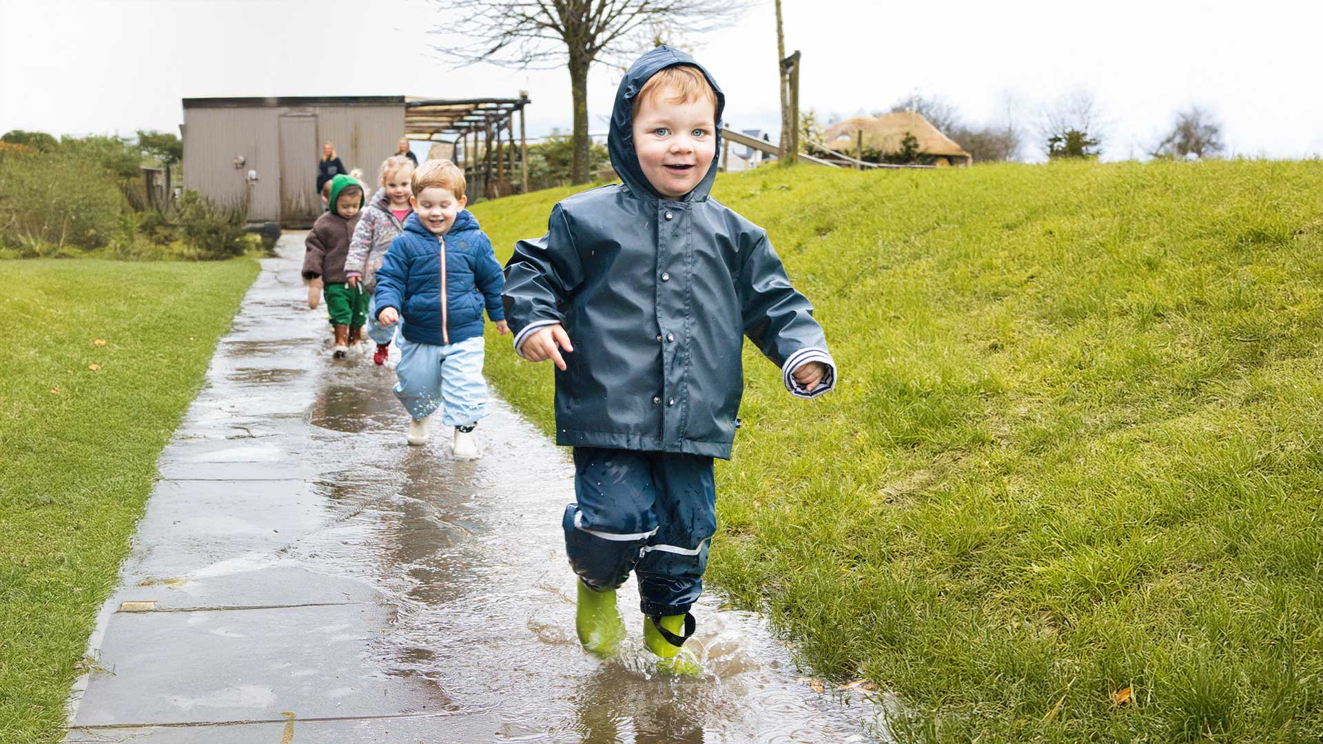 Groep kinderen loopt door plassen tijdens een buitenactiviteit bij Kids Lodge
