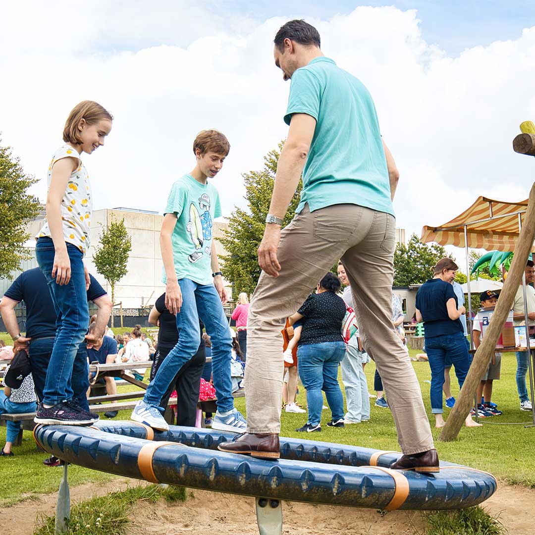 Vader en kinderen balanceren op een speeltuinapparaat tijdens een Kids Lodge event