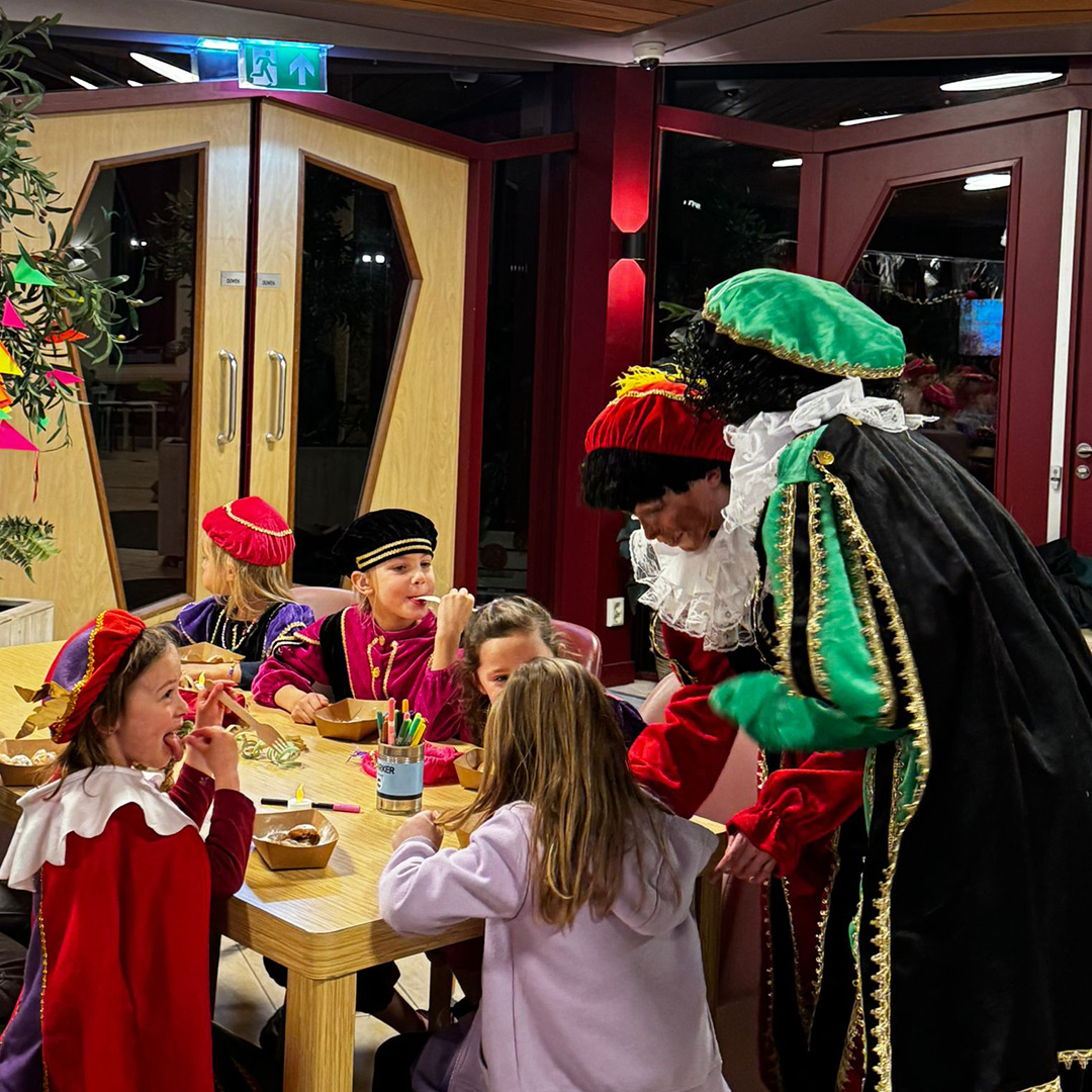 Twee Pieten delen snoepgoed uit aan een groepje kinderen die verkleed zijn als Piet